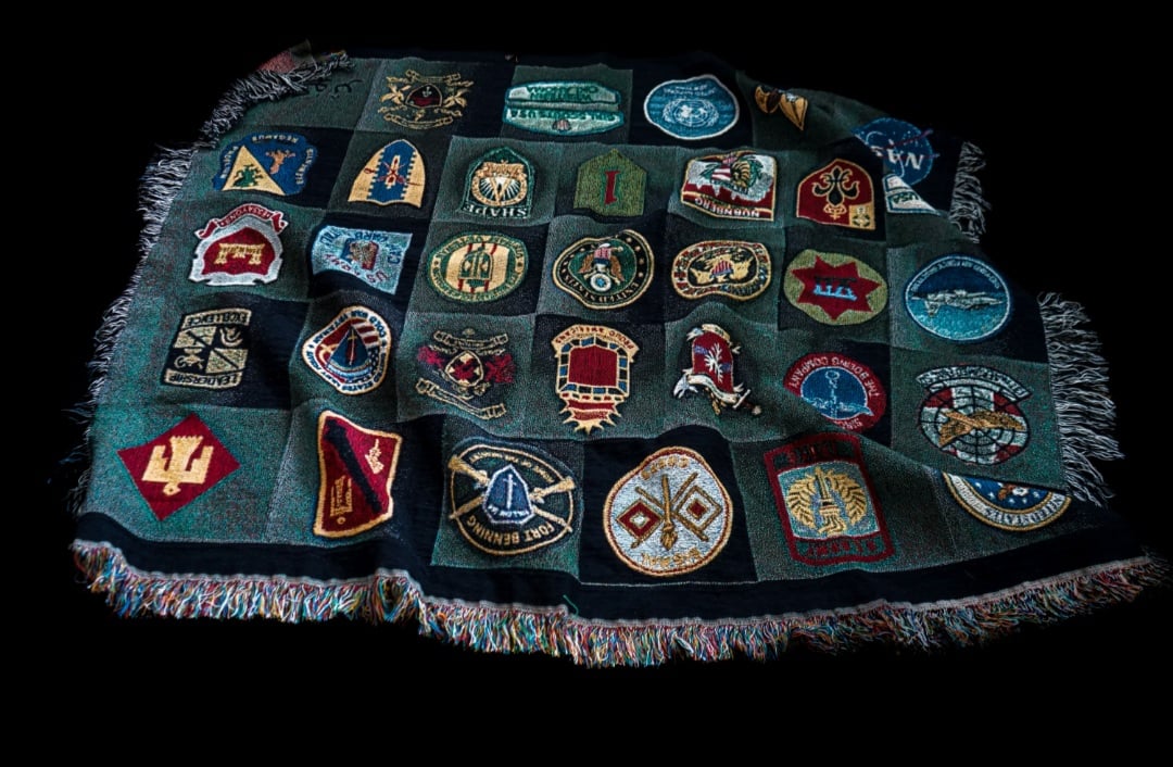 Collection of colorful embroidered band patches arranged on a dark fabric vest or blanket with frayed edges
